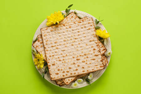 Plate with Jewish flatbread for Passover and flowers on color background