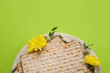 Plate with Jewish flatbread for Passover and flowers on color background