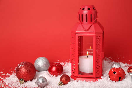 Christmas lantern with burning candle, balls and snow on red background