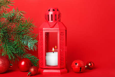 Christmas lantern with burning candle, fir branch and balls on red backgroundの写真素材