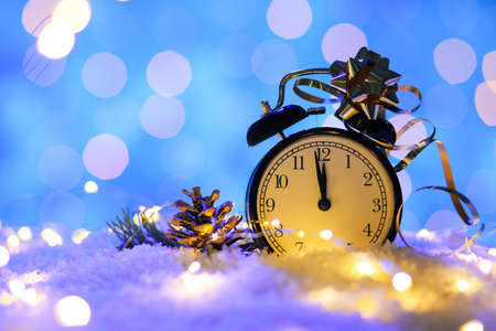 Stylish Christmas clock, decor and snow on table against blurred background