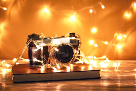 Beautiful Christmas lights, photo camera and book on table near white wallの写真素材