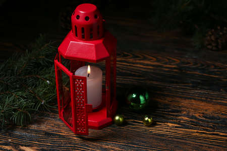 Christmas lantern with burning candle, fir branches and balls on dark wooden background