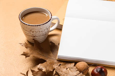 Blank book, cup of tasty coffee and autumn decor on beige backgroundの写真素材