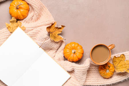Cup of tasty coffee, blank book and pumpkins on beige background