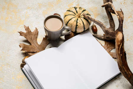 Cup of tasty coffee, blank book and autumn decor on light background