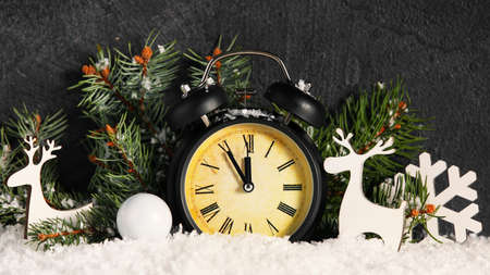 Composition with Christmas alarm clock, Christmas decorations and fir branches on snow against dark...