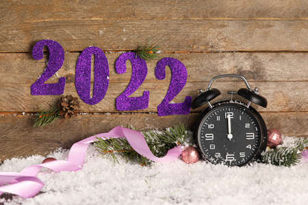 Composition with Christmas alarm clock and figure 2022 on snow against wooden backgroundの写真素材