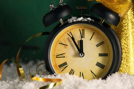 Christmas alarm clock on snow against green background