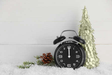 Alarm clock, decorative Christmas tree and pine cone on snow against light wooden backgroundの写真素材