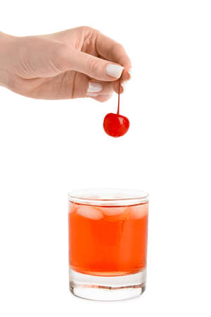 Woman putting cherry in glass of Manhattan cocktail on white backgroundの写真素材