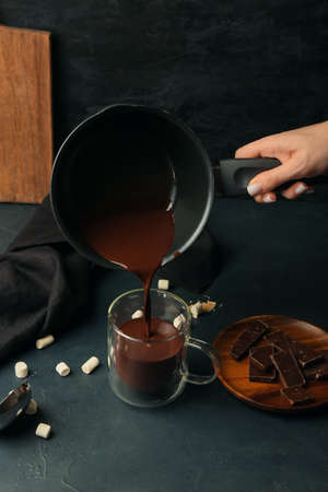 Woman pouring tasty hot chocolate from saucepan into glass cup on black backgroundの写真素材