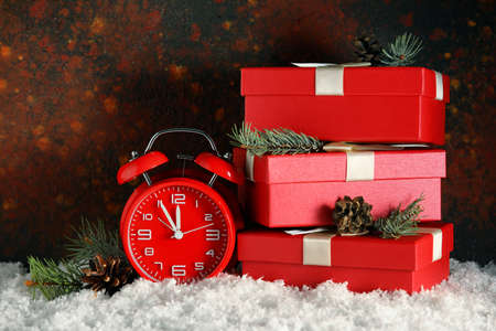 Alarm clock and stack of Christmas gifts on snow against grunge backgroundの写真素材