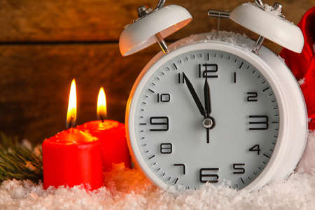 Christmas alarm clock and burning candles on snow against wooden backgroundの写真素材