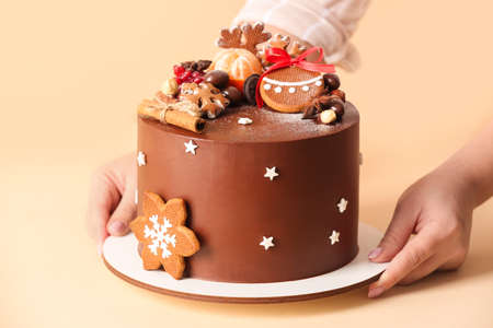 Woman holding stand with tasty Christmas chocolate cake on beige background