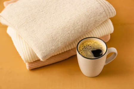 Stack of different cozy sweaters and cup of coffee on wooden background