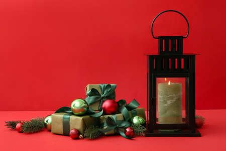 Beautiful Christmas lantern with candle, balls, gifts and fir branches on red backgroundの写真素材