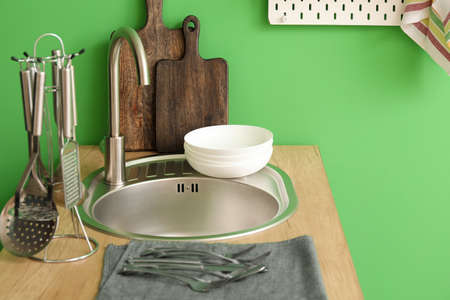 Wooden counter with silver sink and kitchen utensils near green wallの写真素材