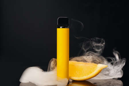 Disposable electronic cigarette and lemon with smoke on dark backgroundの写真素材