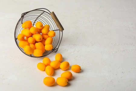 Basket with tasty kumquat fruits on light backgroundの写真素材