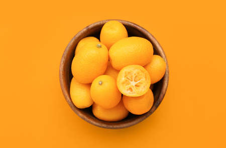 Bowl with tasty kumquat fruits on orange backgroundの写真素材