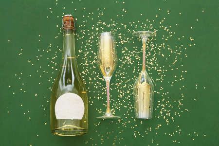 Bottle of champagne with glasses and golden confetti on green backgroundの写真素材
