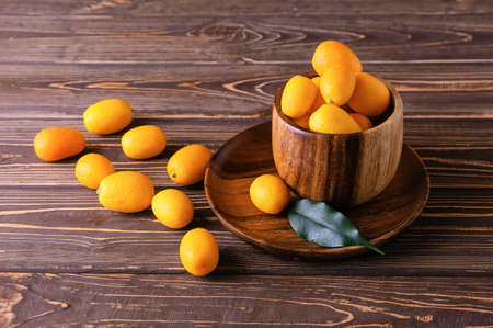 Bowl with tasty kumquat fruits on wooden background