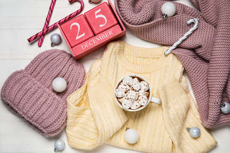 Set of children's clothes, cup of hot chocolate and calendar with date of Christmas on white wooden backgroundの写真素材
