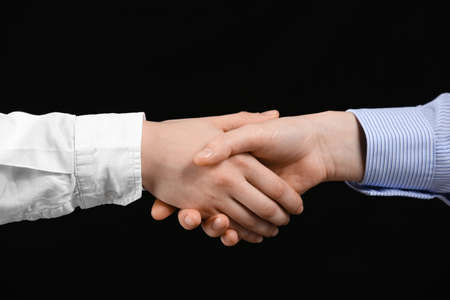 Business woman shaking man's hand on black background, closeup