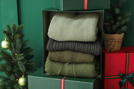 Gift boxes with winter sweaters and Christmas tree near green wall in room
