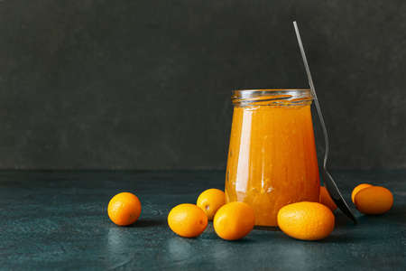 Jar of tasty kumquat jam and fresh fruits on black background