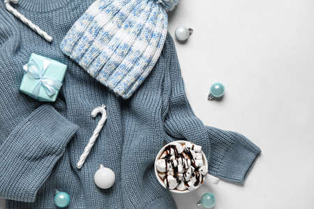 Warm sweater, hat, Christmas decor and cup of hot chocolate on light background