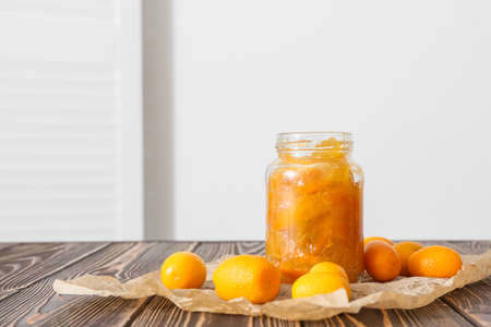 Jar of tasty kumquat jam and fresh fruits on table