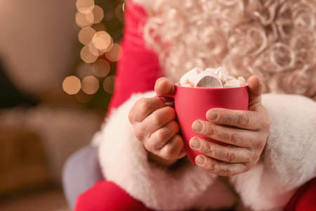 Santa Claus holding cup of hot cocoa with marshmallows in room on Christmas eve, closeupの写真素材