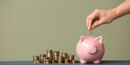 Female hand putting coin into piggy bank on color background. money saving concept