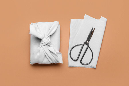 Gift box wrapped in fabric and scissors on color backgroundの写真素材