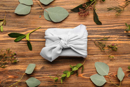 Gift box wrapped in fabric and plant branches on wooden backgroundの写真素材
