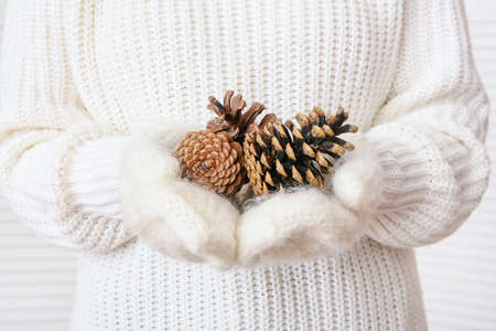 Woman holding beautiful pine cones on light background, closeup