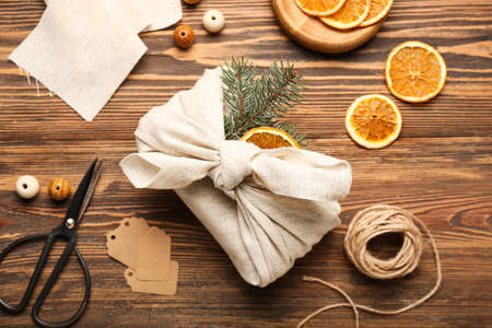 Composition with Christmas gift wrapped in fabric and decor on wooden background
