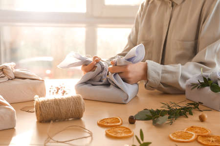 Woman wrapping gift box in fabric on table