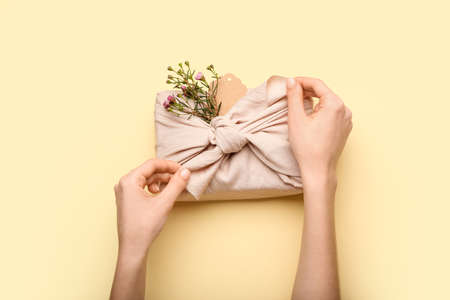Female hands with gift box wrapped in fabric on color background