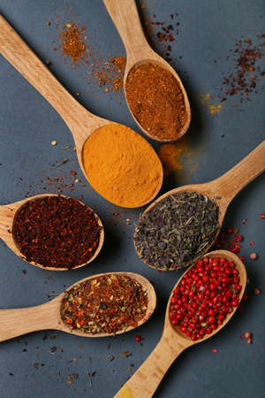 Wooden spoons with aromatic spices on dark background, closeup