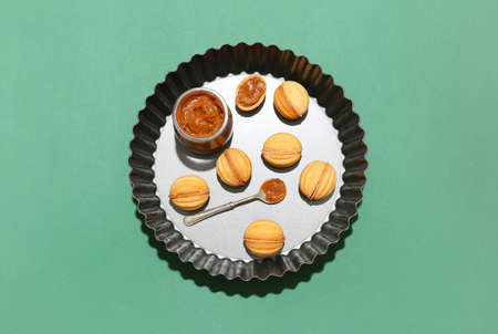 Baking dish of tasty walnut shaped cookies with boiled condensed milk on green background