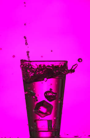 Glass of clear water with splash on color backgroundの写真素材