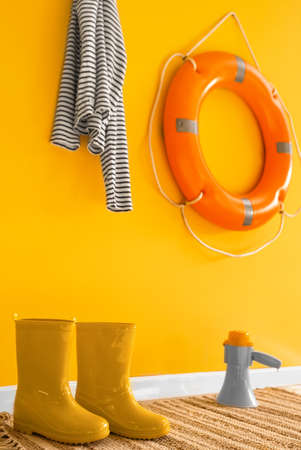 Gumboots, megaphone, sailor's striped shirt and ring buoy hanging on yellow wall