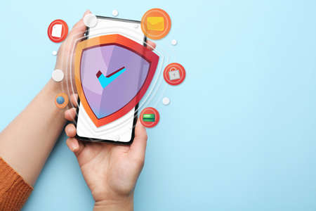 Female hands with mobile phone on light blue background. antivirus conceptの写真素材