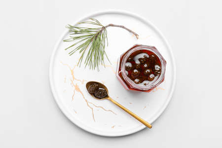 Plate with jar of tasty pine cone jam on light background