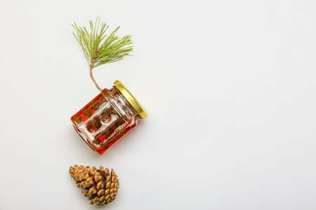 Jar of tasty pine cone jam and fir tree branch on light backgroundの写真素材