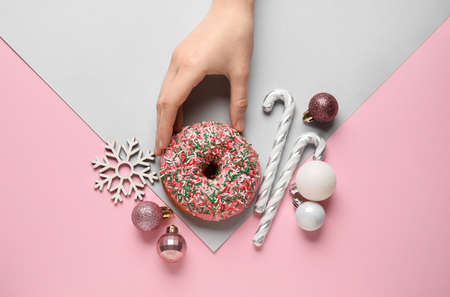 Female hand with tasty Christmas donut and decor on pink backgroundの写真素材