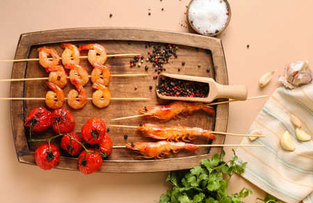 Wooden board with grilled shrimp skewers and tomatoes on beige backgroundの写真素材